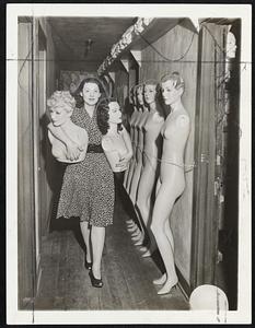 Incident in Mannequin-Works--Katherine Stubergh carries likenesses o Marlene Dietrich and Hedy Lamarr. A row of wax mannequins seem to be watching. Stubergh mannequins have faces like movie stars but are all alike from the neck down.