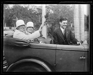 Three people seated in a car, one waving