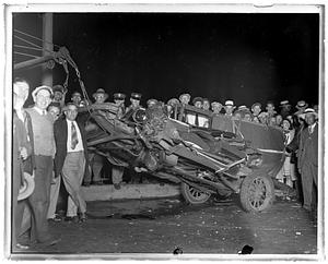 People stand by a wrecked car about to be towed away