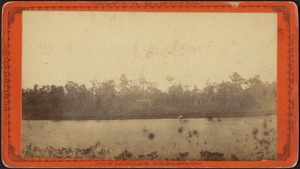 View of an unidentified body of water (in foreground) and a house partially visible on the opposite shore