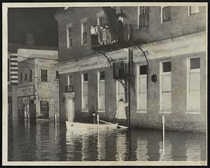 Safe Step in the Flood- A rescue boat comes alongside as man swings from fire escape ladder on Foster street in flood-washed center of Peabody where 30 families were saved. Others wait turn on fire escape above. A Coast Guard amphibious duck completed the rescue a short time later.