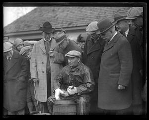 A seated man, holding a fish, surrounded by a crowd