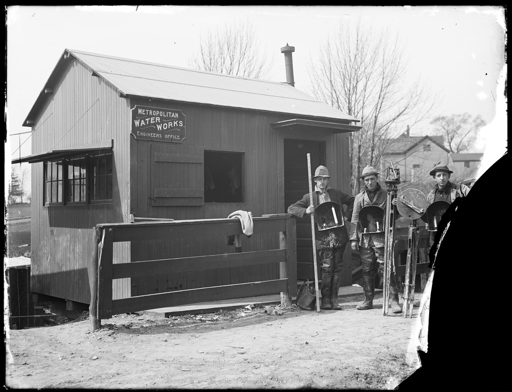 Metropolitan Water Works Miscellaneous, Engineers Office, sign on small building, "Metropolitan Water Works Engineers Office"; 3 engineers standing in front with surveying equipment, likely after working in the aqueduct tunnel, Northborough?, Mass., ca. 1895-1899