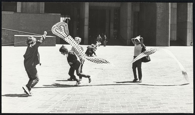 At City Hall Plaza – Children duck, as kite comes shooting down from gust of wind.