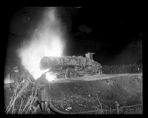 Unidentified truck on fire, firefighters with hoses in foreground, spectators in background