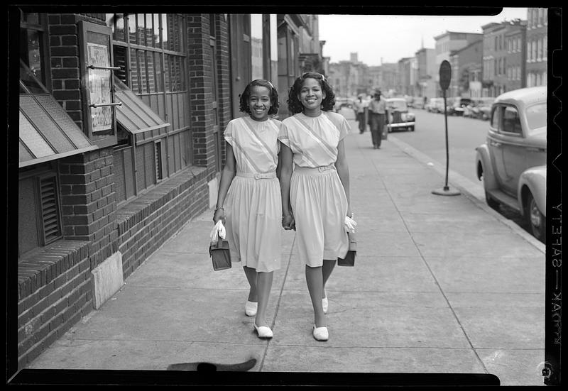 Two young women walk down a sidewalk