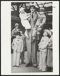 Quite A Family? You’re wrong. It looks like papa and the children, but it’s really Dinny Duffy, 8-foot Australian giant, and a party of Fred Roper’s midgets, who left London recently for South Africa.