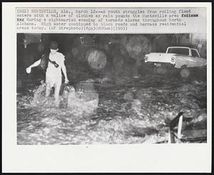 Huntsville, Ala. -- A youth struggles from roiling flood waters with a valise of clothes as rain pounds the Huntsville area during a nightmarish evening of tornado alarms throughout North Alabama. High water continued to block roads and harass residential areas today.