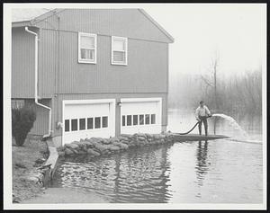 Pumping the Concord River out of his cellar is T. Robert Primmerman of 16 Sheridan Rd., Bedford. Like many of his neighbors, Primmerman had to evacuate his family because of the flood.