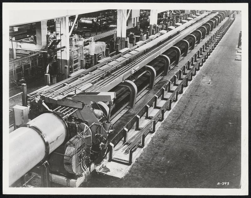 By Chase Brass & Copper Co.-This huge machine (note the man at far left) can draw a 210-foot long straight copper tube with an outside diameter of from 1/2 to 2 inches. Five tubes can be drawn at once, with a force of 150,000 pounds.