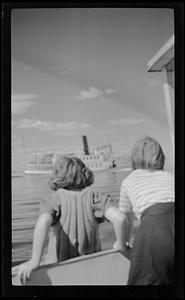 Two children facing away from the camera looking at ship on water