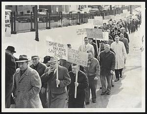 Members of New Haven's Brotherhood of Railroad Trainmen start march to State House from Dewey Sq. today carrying placards (left photo). At right, they parade up Park St. side of Common. They are backing Gov. Volpe's recommendation for state aid for the rail line.
