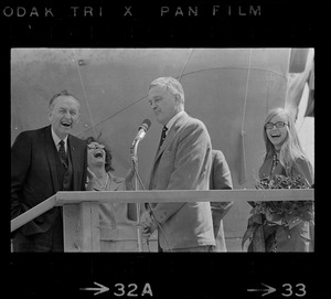David S. Lewis, head of General Dynamics, speaking at christening ceremony for the USS Mount Vernon with others in background laughing, including Barry J. Shillito, Assistant Secretary of Defense and his wife, far left