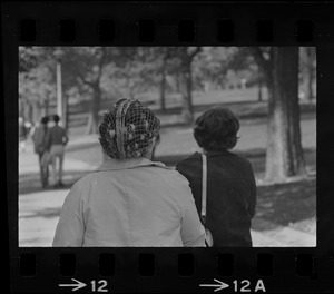 Two women, one with hair curlers, walking outside and seen from behind