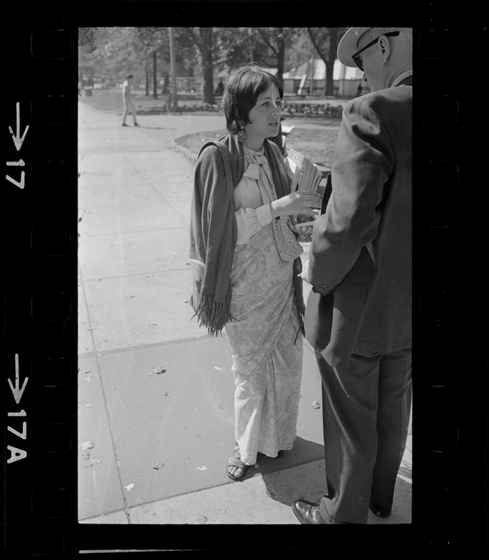 A woman talking with a man and holding a stack of pamphlets of A.C. Bhaktivedanta essays