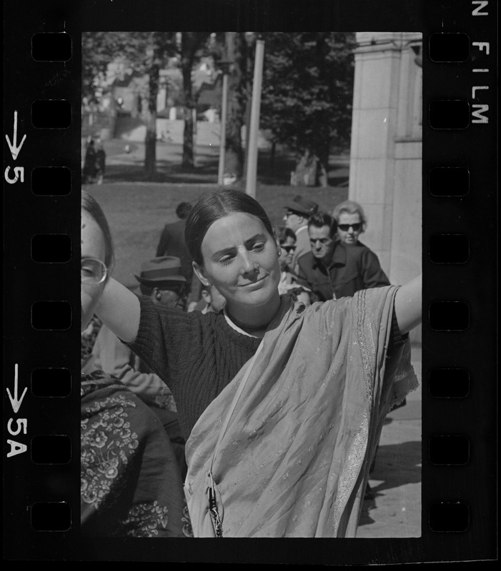 A woman with a scarf wrapped around her and holding her arms open wide