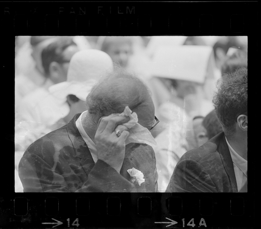 Audience member at Brandeis University commencement wiping his brow, presumably due to the heat