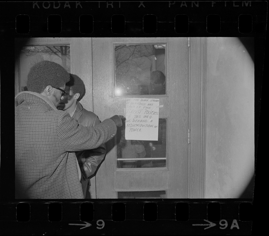 Black students at Brandeis University stand outside door of Ford Hall during protest and read sign listing demands