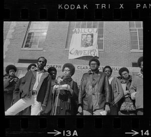 Surrounded by backers, Sharon Hammond of Boston, a sophomore at Brandeis University, speaks beneath the banner of Malcom X University, the name given to Ford Hall by Black students demanding Black instructors for Black oriented courses