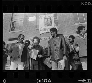 Surrounded by backers, Sharon Hammond of Boston, a sophomore at Brandeis University, speaks beneath the banner of Malcom X University, the name given to Ford Hall by Black students demanding Black instructors for Black oriented courses