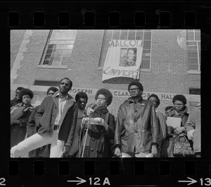 Surrounded by backers, Sharon Hammond of Boston, a sophomore at Brandeis University, speaks beneath the banner of Malcom X University, the name given to Ford Hall by Black students demanding Black instructors for Black oriented courses