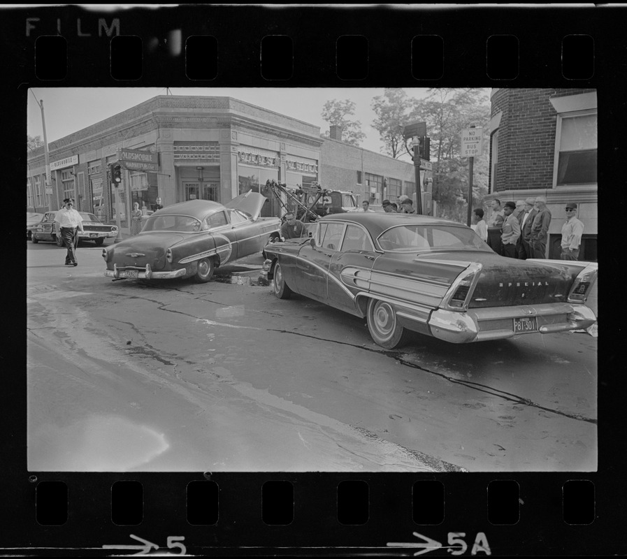 Two cars, one being towed, on street corner near Barnett Motors Oldsmobile dealership