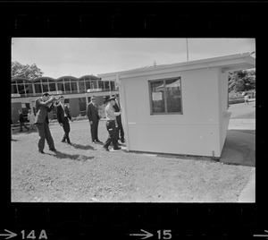 Photographer photographing group of men standing outside and looking into small building on Brandeis University campus on day of commencement