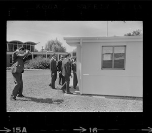 Photographer photographing group of men standing outside and looking into small building on Brandeis University campus on day of commencement