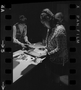 Wife of serviceman believed to be POW's being held by Communists, Mrs. Joseph Dunn, Randolph (believes husband was shot down over China) looks at photographs while preparing to hang a poster in Boston City Hall