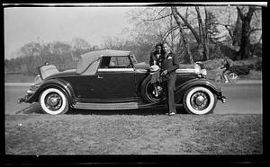 Constance Miller sits on car hood holding a hat while posing with a man