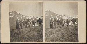 One woman and six men stand, mountains in background