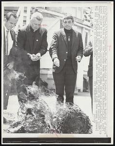 Baltimore, MD.: Two Catholic Priests watch two baskets of draft board records burn after the records were taken from the Catonsville, Md. draft board office by nine persons, including five Roman Catholic priests. Father Philip Berrigan (L), who was involved with the pouring of blood on draft records 10/67, and his brother, Rev. Daniel Berrigan were arrested along with the seven others. The man at left is unidentified.