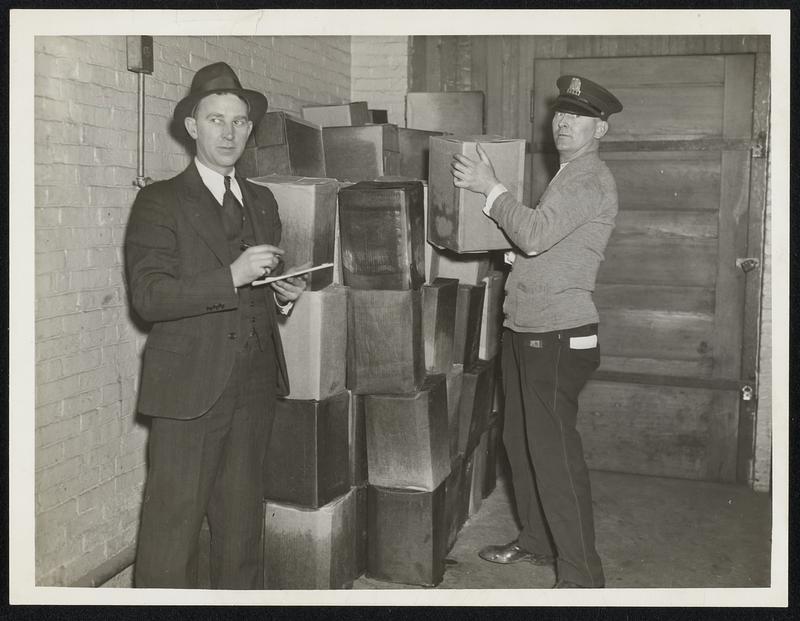 Patrolman Thom J. Lowndergan piling cans of alcohol as Patrolman Edw. J. Curtis of liquor squad checks