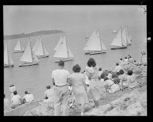 Spectators watch yachts sail out of harbor