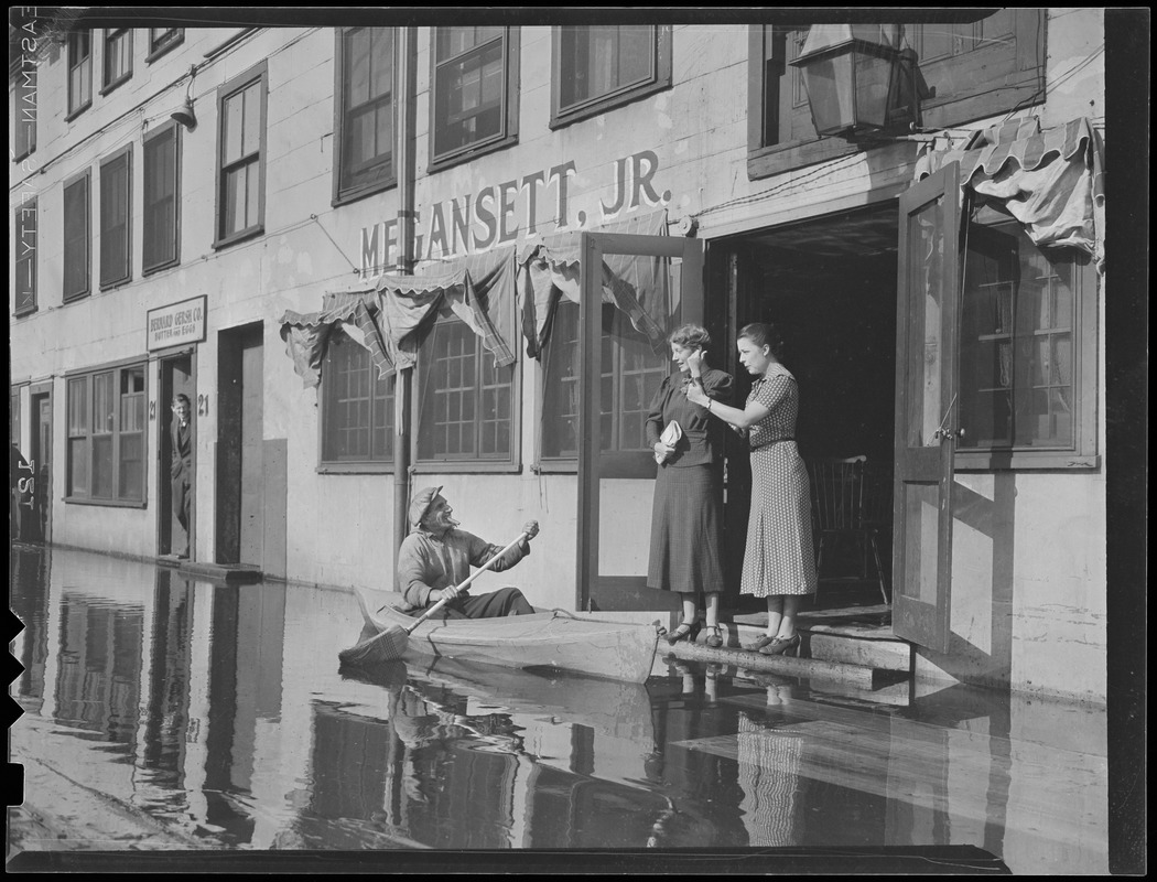 Man in rowboat in front of Megansett, Jr. restaurant, flooded T-wharf