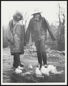 Two girls in raincaots and boots standing in water