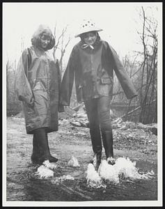 Two girls in raincoats and boots standing in water