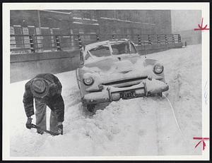 Motorist stranded on Southeast Expressway starts chilly task of shoveling out car. Similar scenes occurred throughout city.