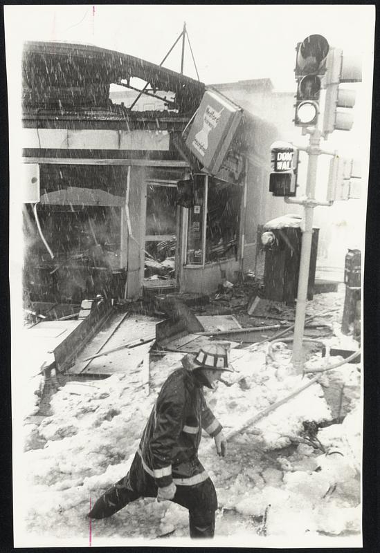 Firefighter wades through deep water and slush in front of Medford business block destroyed by fire during yesterday's storm.