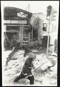 Firefighter wades through deep water and slush in front of Medford business block destroyed by fire during yesterday's storm.