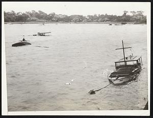 Some of the capsized and partly sunken boats which were left in the waters off Fore River bridge early yesterday morning as the tail of the hurricane lashed the Massachusetts coast. In the upper left corner of the picture is an owner in a row boat trying to pull his overturned sailboat to shore.