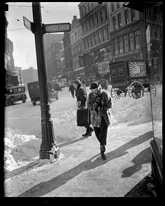A woman walking through snowy streets at the corner of Church Green and Summer Street, Boston