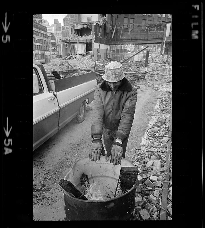 Demolition worker warms hands at oil-drum fire on winter day, Boston