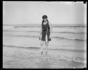 A woman stands in the water at the beach in a bathing costume