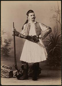 Studio portrait of man in traditional Greek dress with rifle and sword