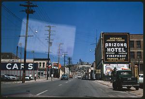 View down street past Arizona Hotel sign toward hill with mine head frame, Butte, Montana