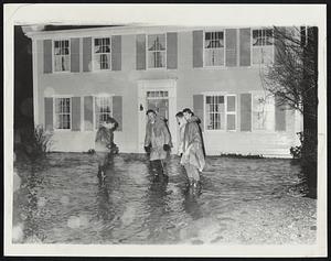 Four men in raincoats and boots standing in floodwater in front of house
