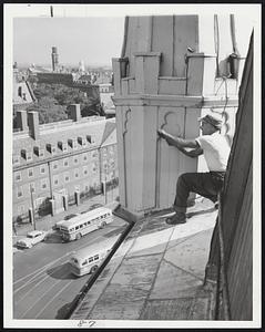 At right, John Gilbert of Dorchester works on the tower 100 feet above Harvard square. The historic First Parish "Meeting House" was build in 1832.