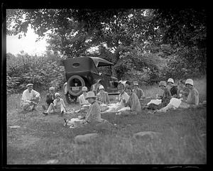 A group of people picnicking, an automobile in the background