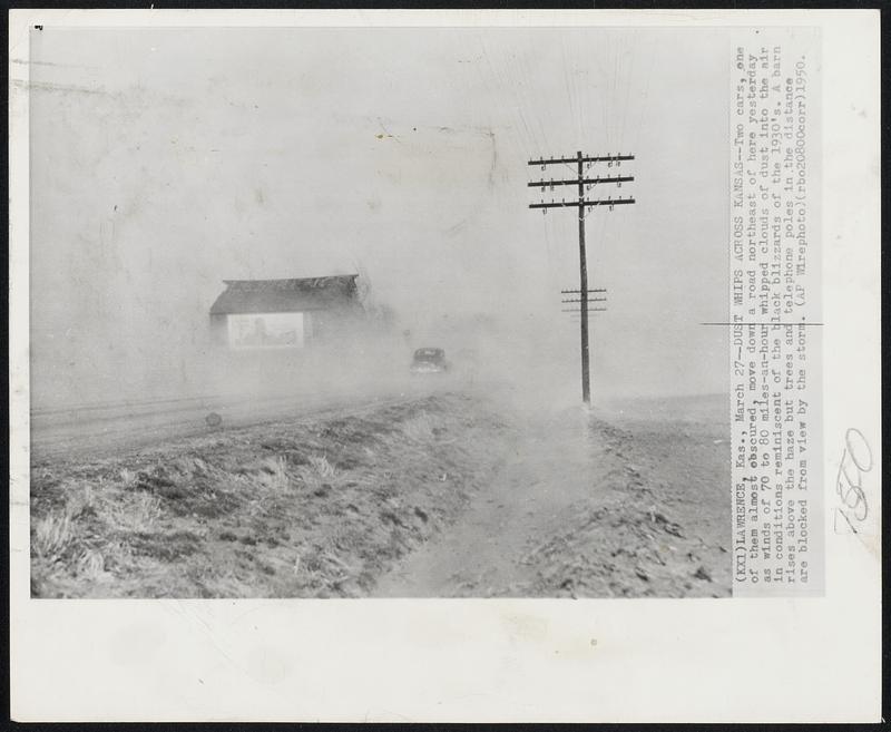 Dust Whips Across Kansas -- Two cars, one of them almost obscured, move down a road northeast of here yesterday as winds of 70 to 80 miles-an-hour whipped clouds of dust into the air in conditions reminiscent of the black blizzards of the 1930's. A barn rises above the haze but trees and telephone poles in the distance are blocked from view by the storm.